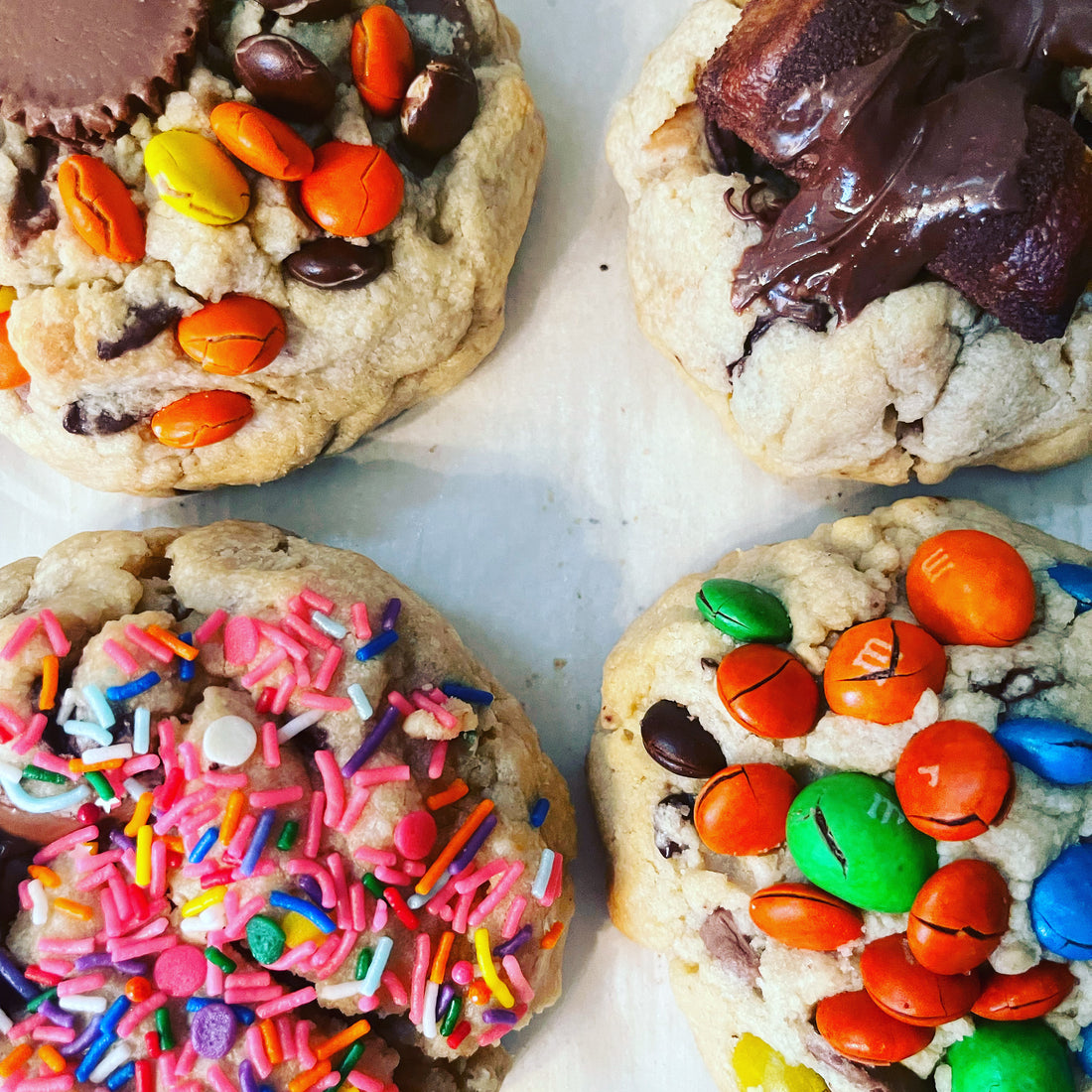 4 cookies, one with sprinkles, one with Reese’s pieces and mini Reese cup, one with bueno wafer covered in chocolate, and one M&M cookie